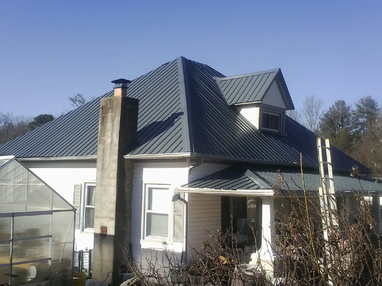 Dark blue standing seam metal roof on a white farmhouse with dormer — Slate & Tile Roof Repair by Roofing Brothers in Monument