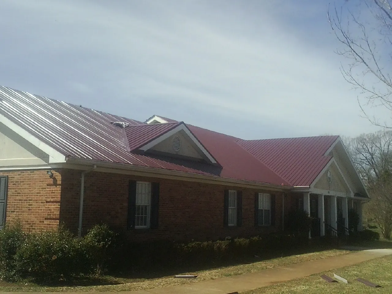Red metal roof with gabled entries on a long brick building, from a Hail Damage Roof Repair job in Monument
