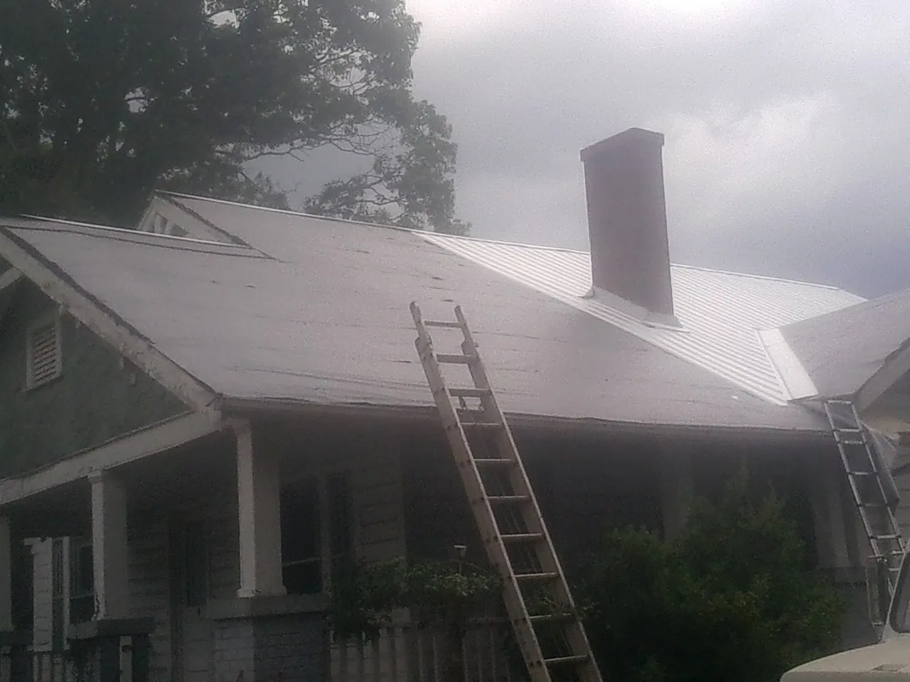 Ladders against a metal roof on an older home with a brick chimney in Monument