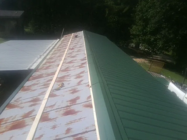 Old rusted panels beside newly installed green metal roofing — Wind Damage Roof Repair by Roofing Brothers in Monument