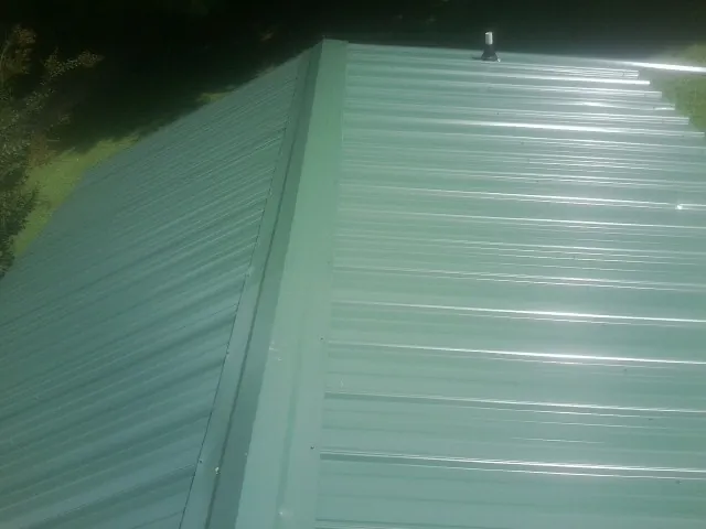 New green metal panels meeting at the ridge of a roof — Flat Roof Repair work by our crew in Monument