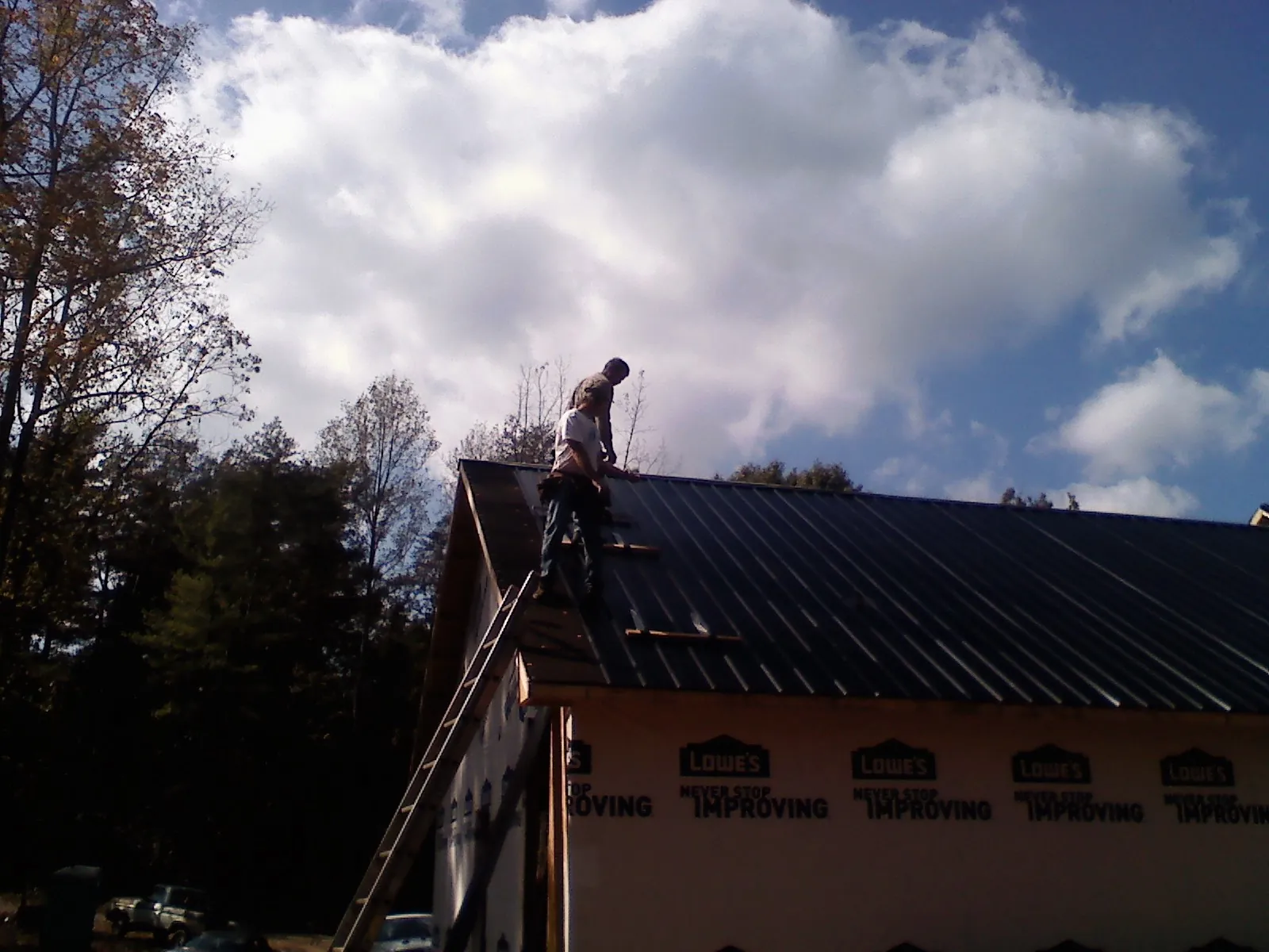 Roofer fastening dark metal panels high against a cloudy sky, from a Roof Inspection job in Monument