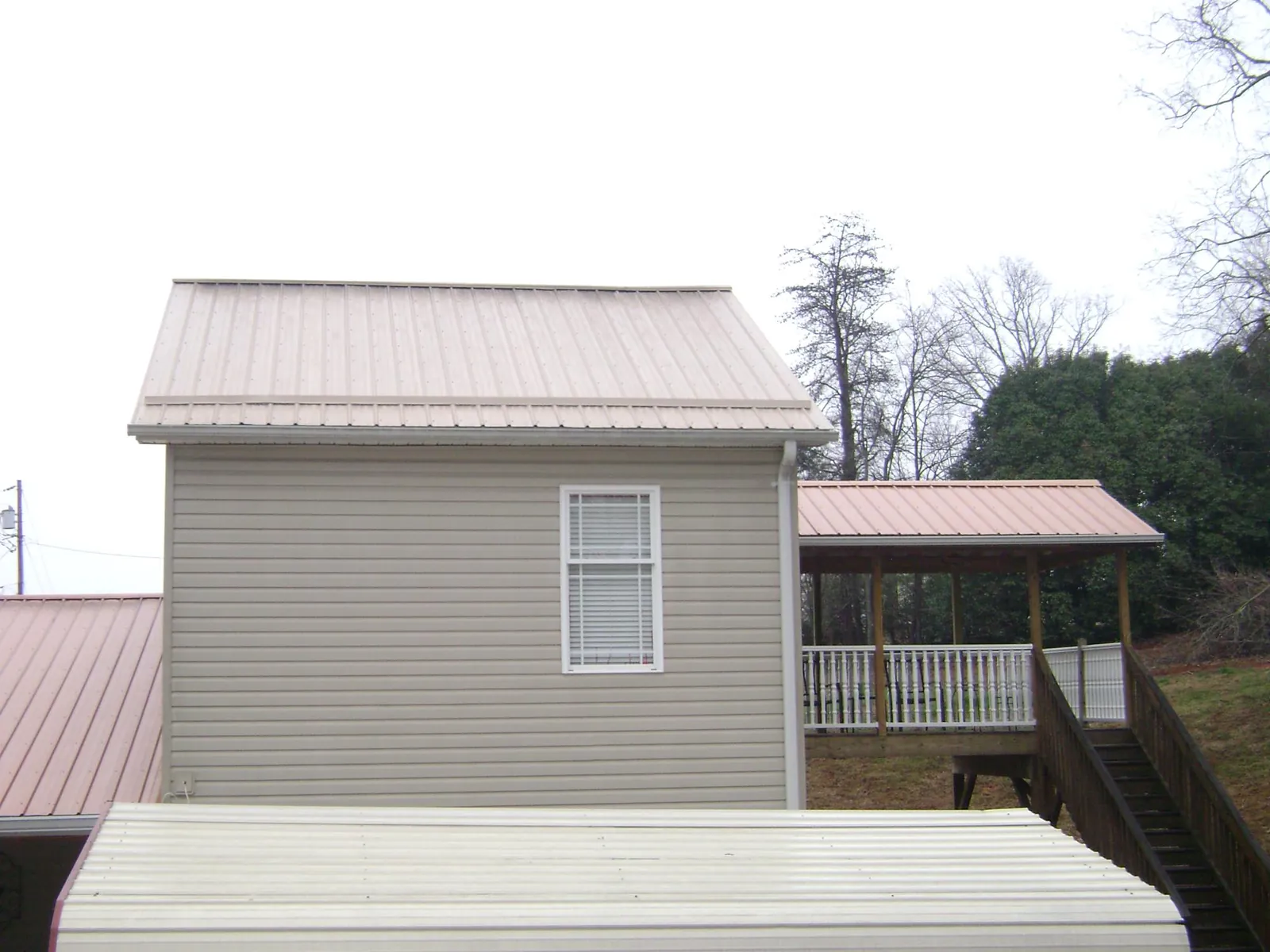 Tan metal roofs on a two story addition and attached porch, from a Roof Replacement job in Monument